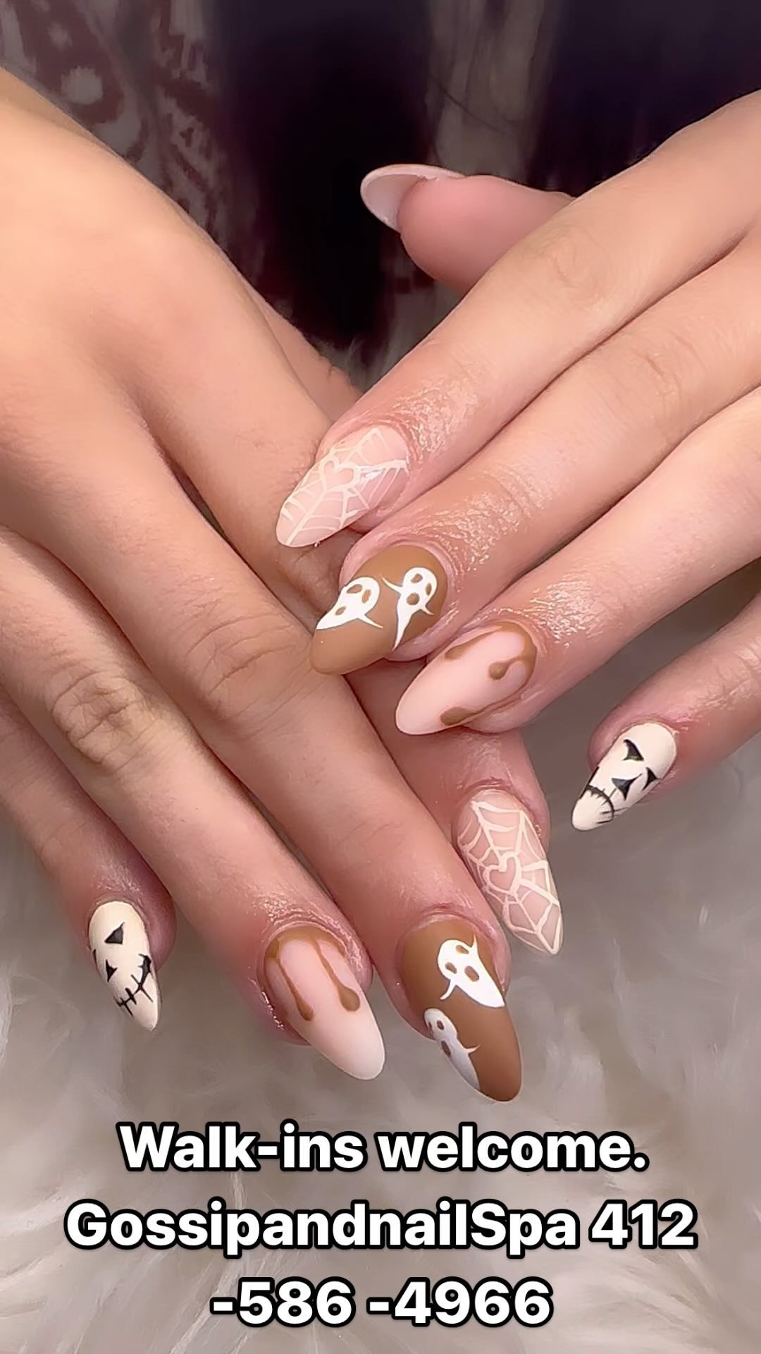 Nude almond nails with white ghosts, caramel drips, spiderwebs and stitched jack-o’-lantern faces