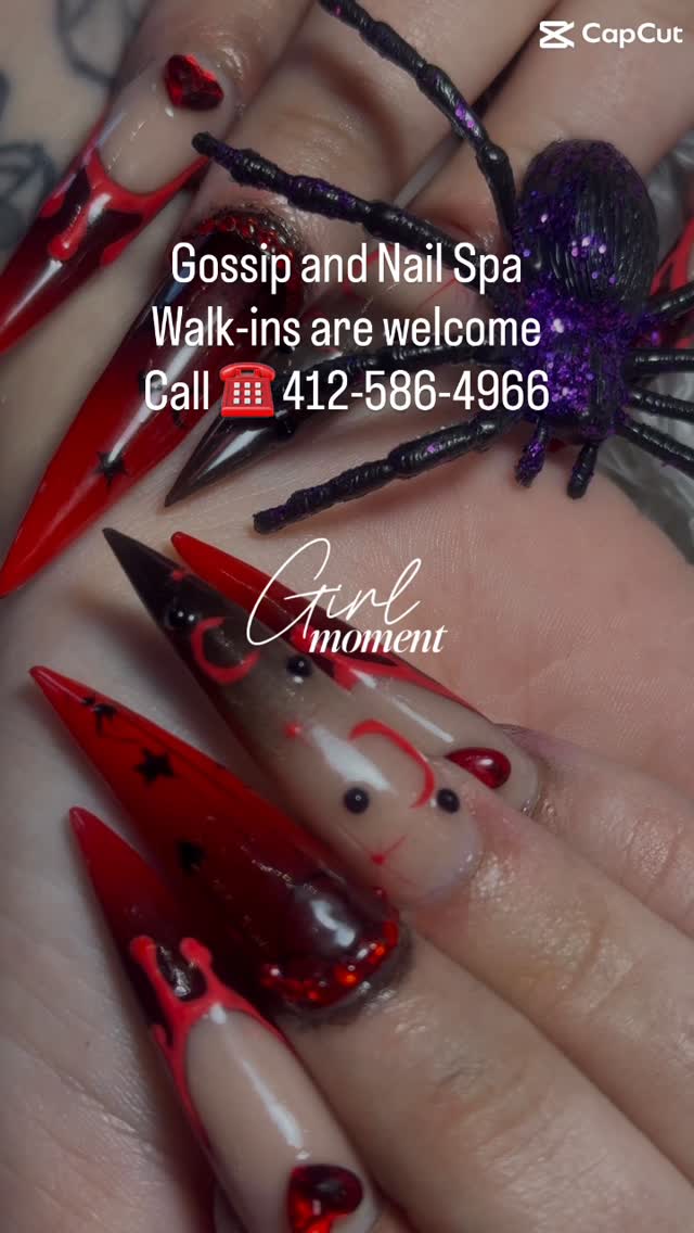 Long red and black stiletto nails with red drips, black stars and red gem hearts, next to a glitter spider